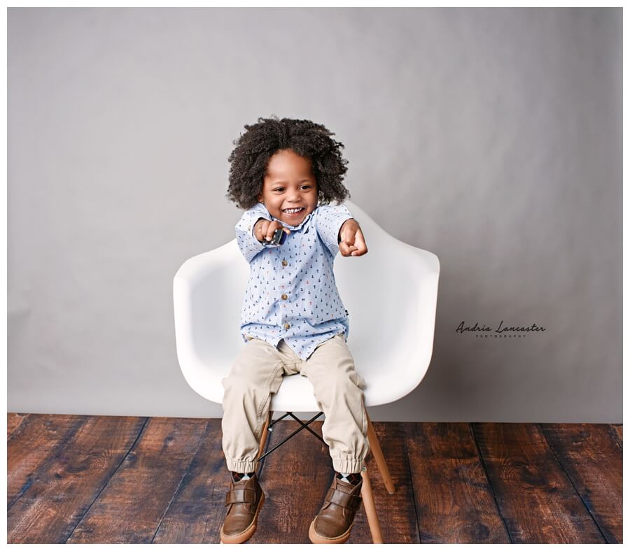 2 year old sitting on a white chair pointing at camera