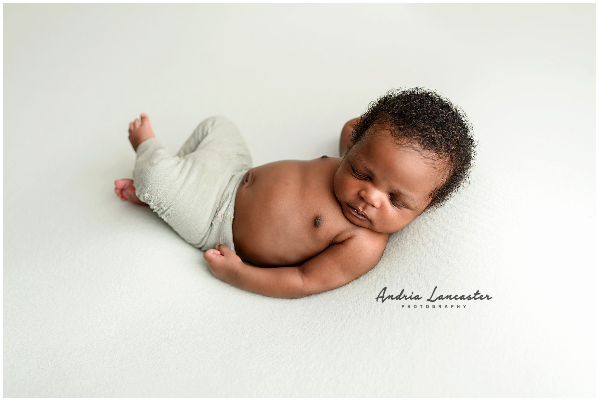 Newborn laying on back with hands to the side wearing green pants