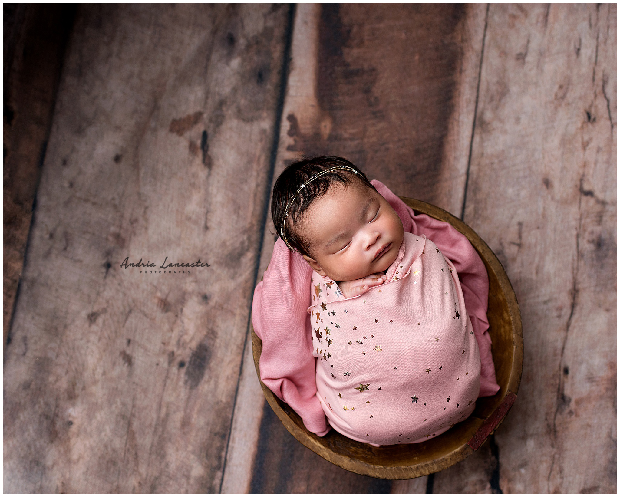 Newborn wrapped in pink with star headband in a bowl