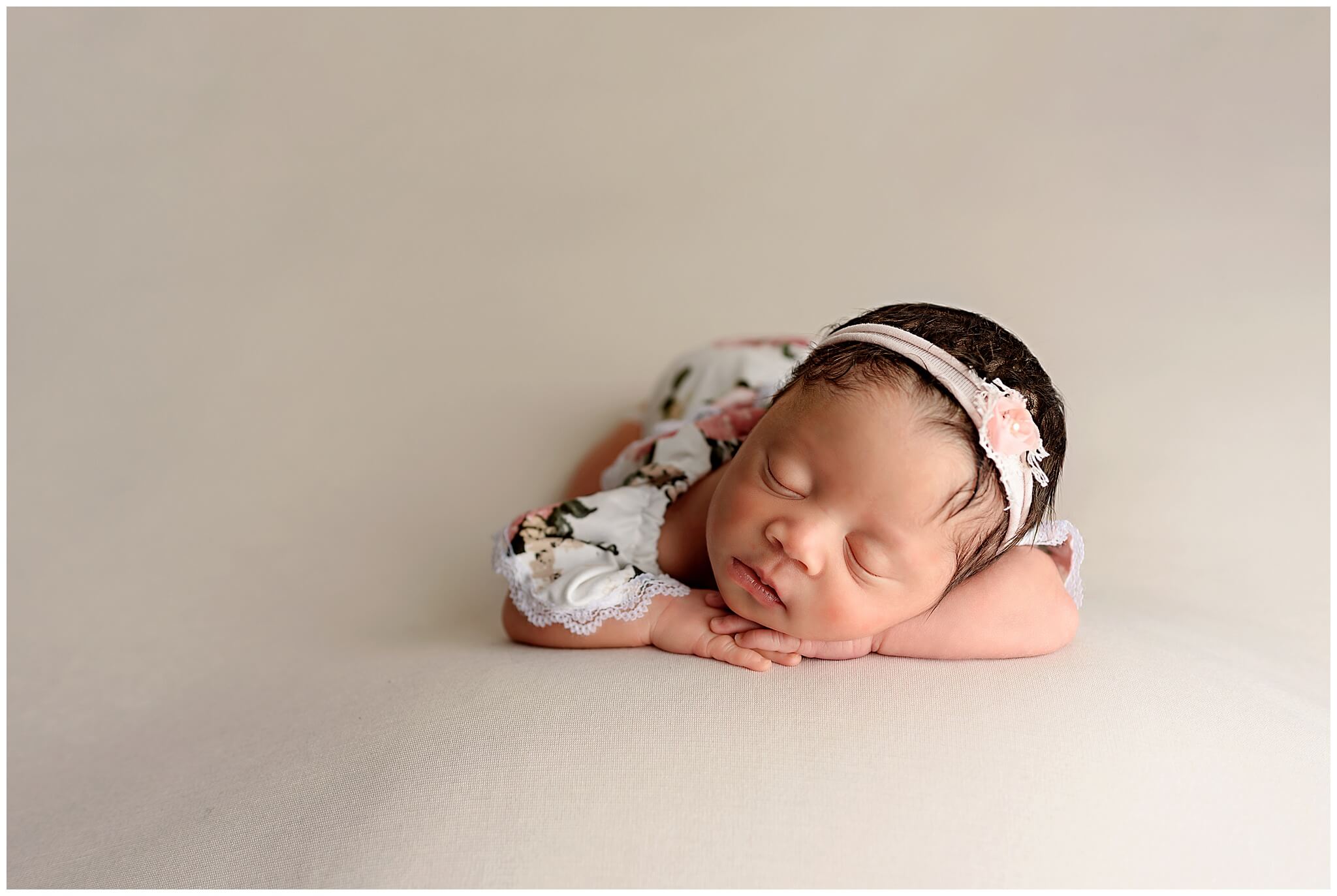 baby wearing pink headband laying chin on hands