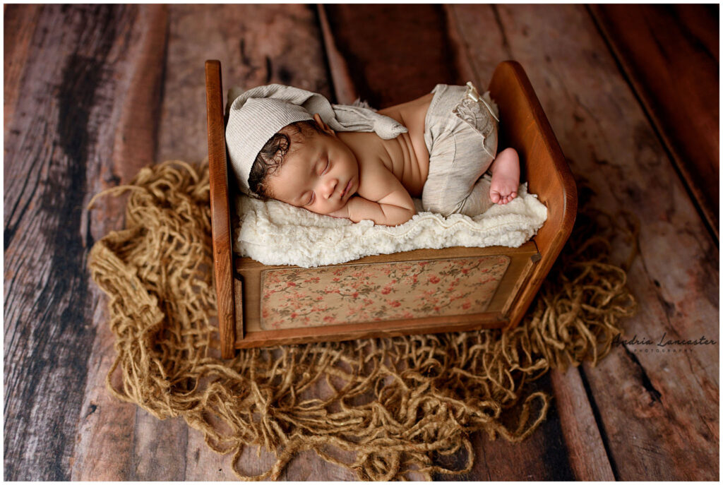 newborn posed on bed wearing pants with bow and sleepy cap