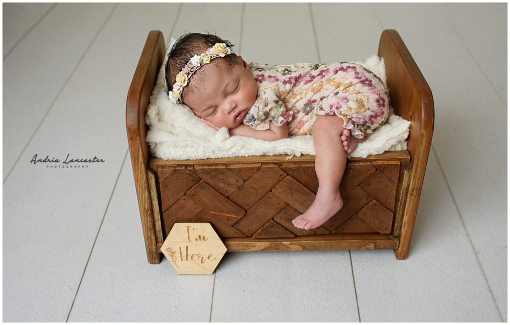 newborn in wooden bed prop with one leg of bed