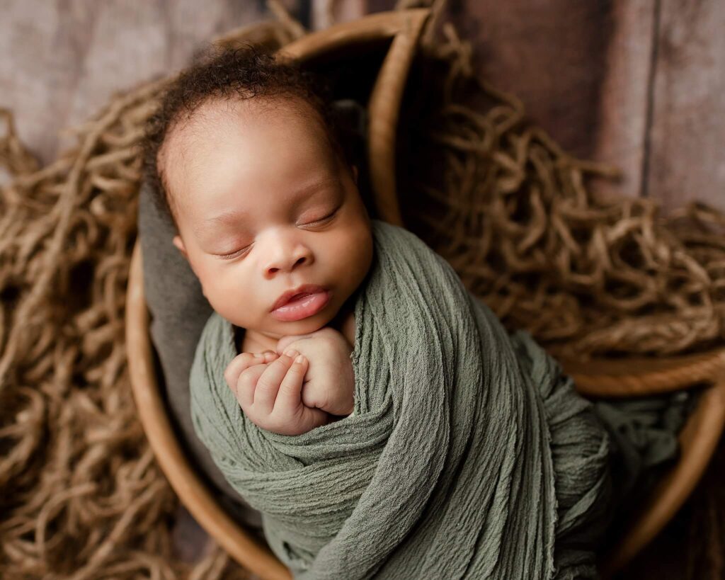 A newborn baby boy wrapped in soft green wrap in moon bowl prop