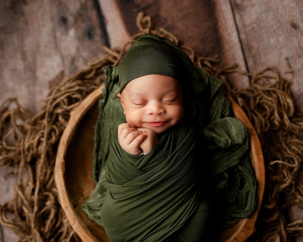 A precious newborn baby wrapped in a cozy green wrap with hands out