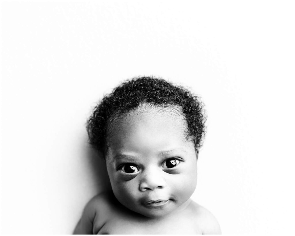Black and white image of baby boy looking at camera with his big beautiful eyes.