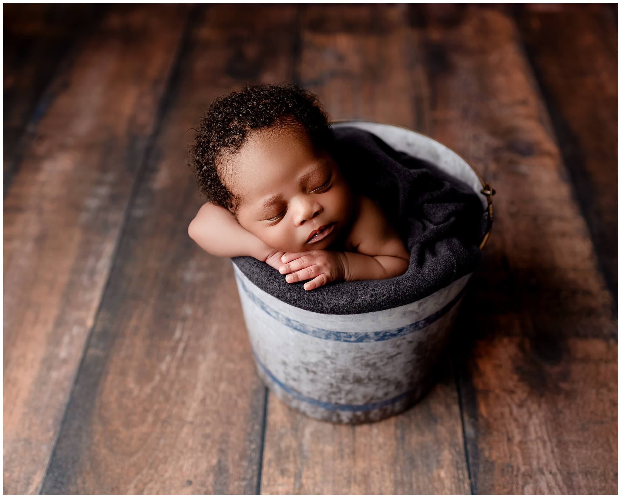 Newborn bucket prop with baby boy sleeping soundly with his head laying peacefully on his arms.