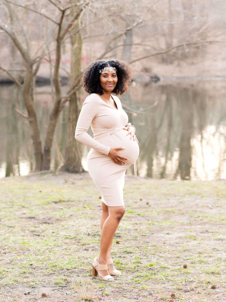 Pregnant woman standing facing the right with her hands on her belly. She is facing the camera.