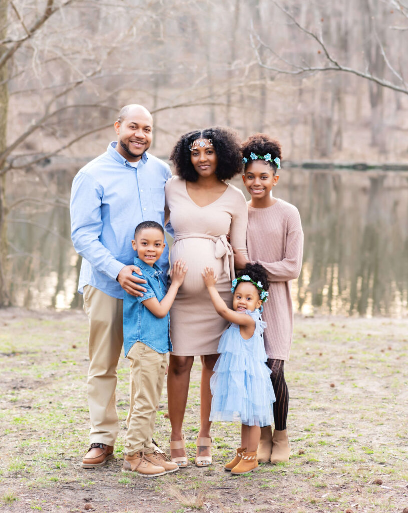 Family maternity session in prospect park Brooklyn NY. Family of 5 standing together with father on one side of mom and the older child on the other side. The two smaller children standing in the front with both of their hands on moms belly.