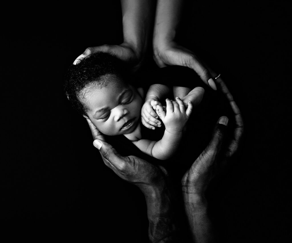 Baby wrapped in black wrap with parents hands on top and bottom of the image showing parents holding her up.