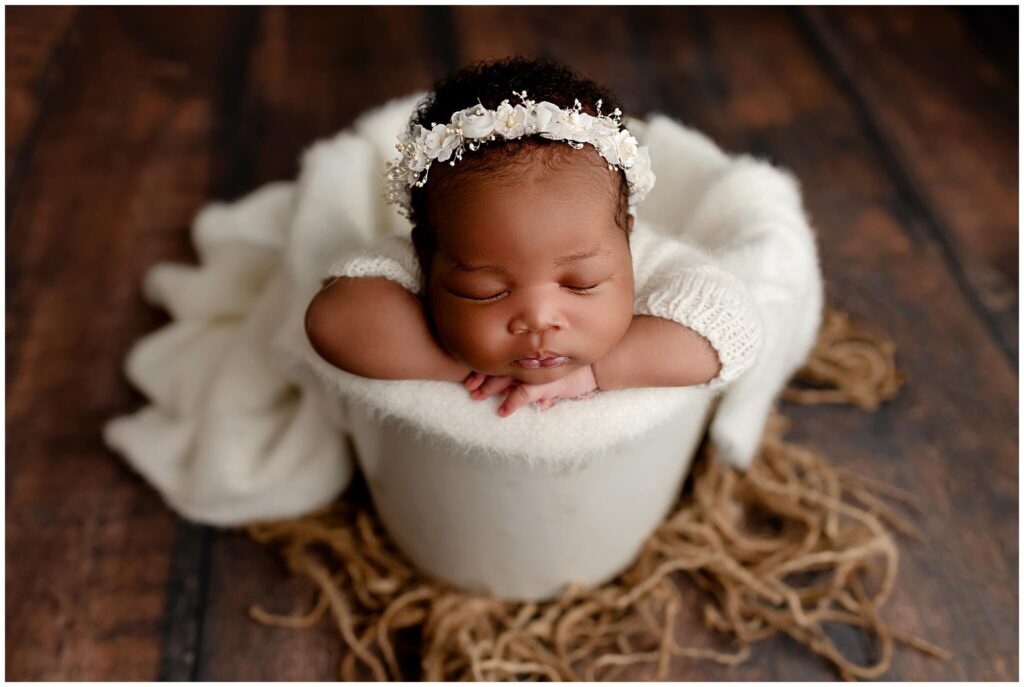 Newborn baby girl wearing a white floral headband in bucket pose.