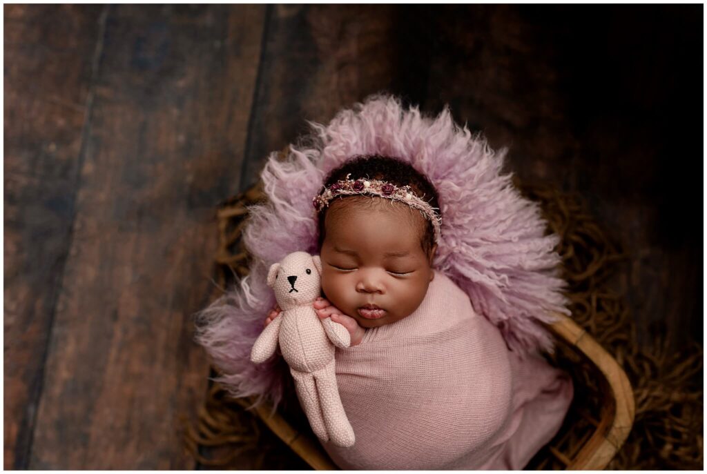 Newborn baby girl with pink floral headband holding a teddy bear.