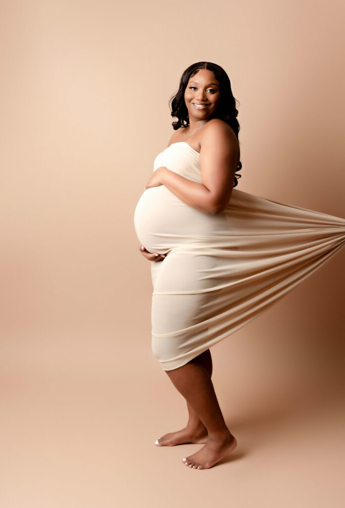 Pregnant woman draped in white cream silk and it is pulled back to show her belly.