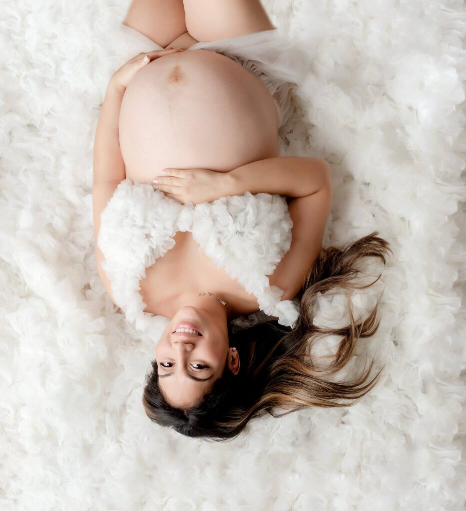 Pregnancy photos with mom laying on her back on a pillow of white fabric.