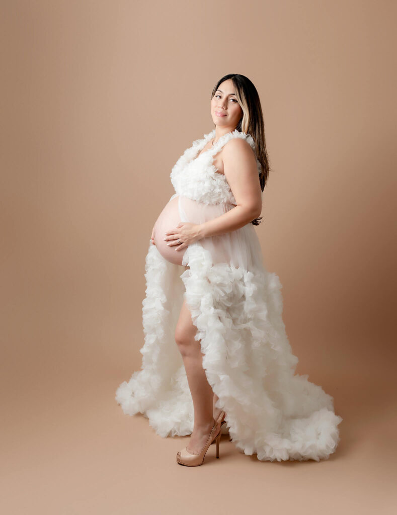 Maternity image of a mother wearing heels and standing holding her belly.