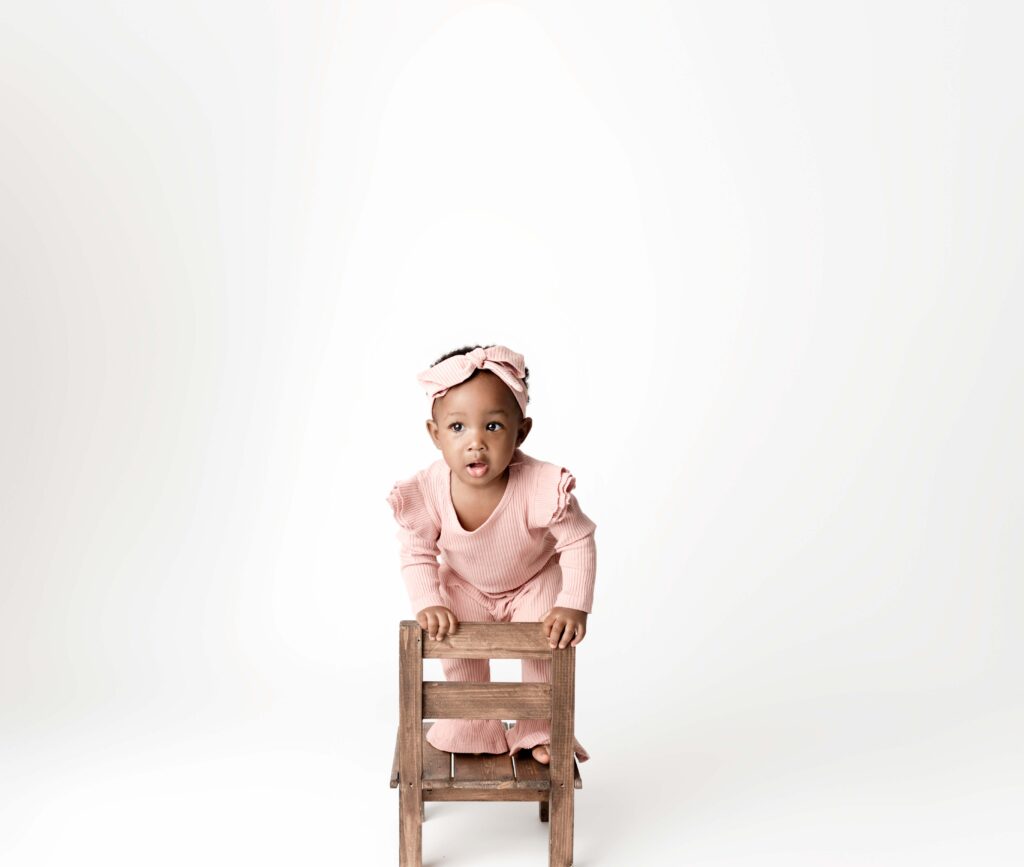 One year old baby girl photo session standing on a little chair.