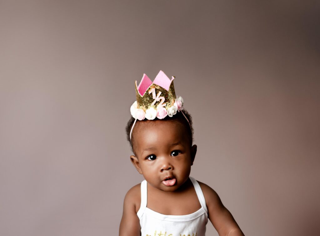 6 month old baby girl wearing a 1/2 year crown and looking at the camera.