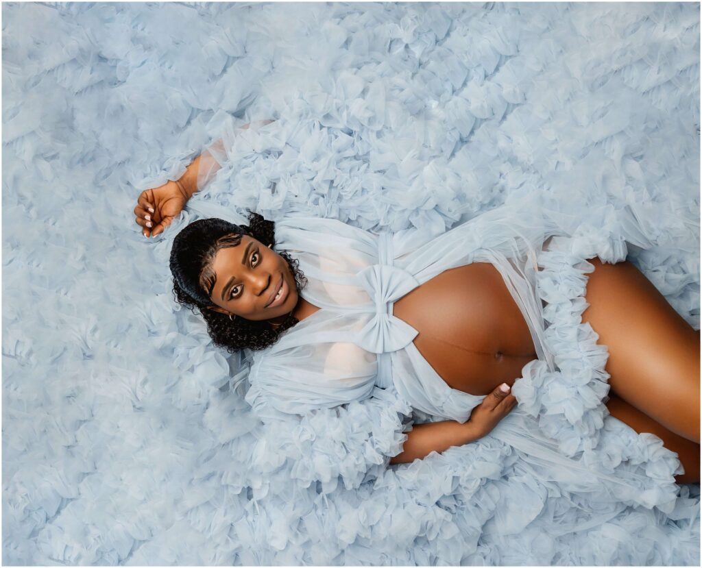 Maternity portrait of woman laying down in large fluffy dress fabric. Amazing baby shower backdrop portrait.