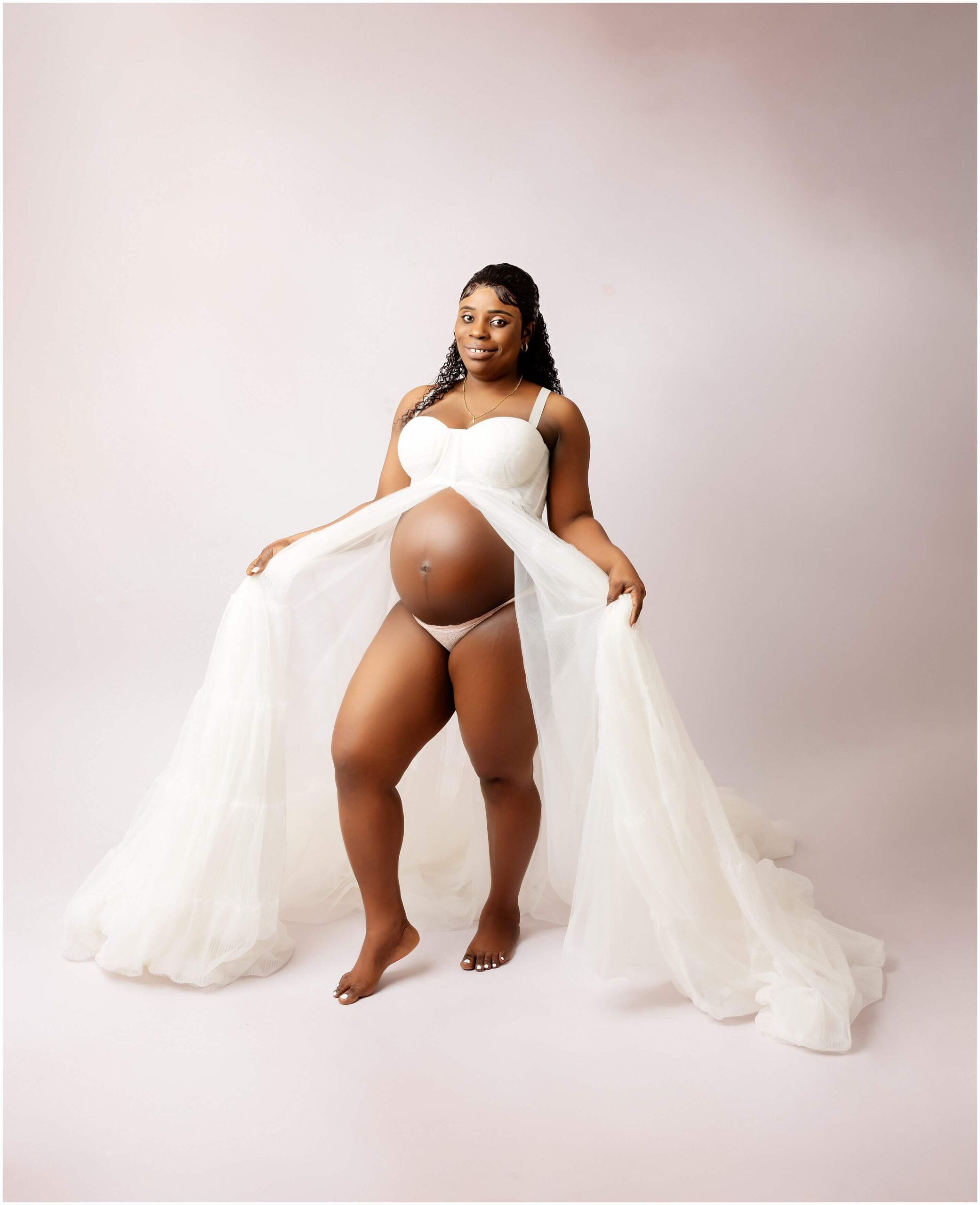 Smiling pregnant woman wearing white dress on a cream backdrop. Maternity Portrait that can be used at baby shower.