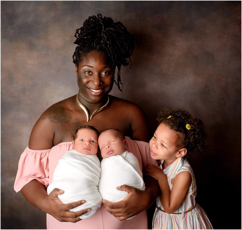 Mother holding her twin boys while their sister looks sweetly at them. One baby is asleep and the other is wide awake.